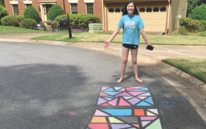 A girl showing off her colorful, geometrical sidewalk chalk art.